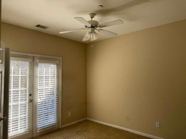 carpeted empty room with a ceiling fan, baseboards, visible vents, and french doors