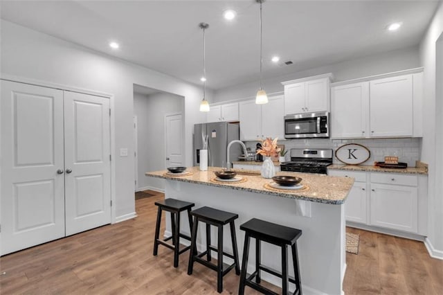 1311 Park Center Cir, Austell, GA 30168 - kitchen featuring appliances with stainless steel finishes, white cabinets, a kitchen breakfast bar, tasteful backsplash, and a kitchen island with sink