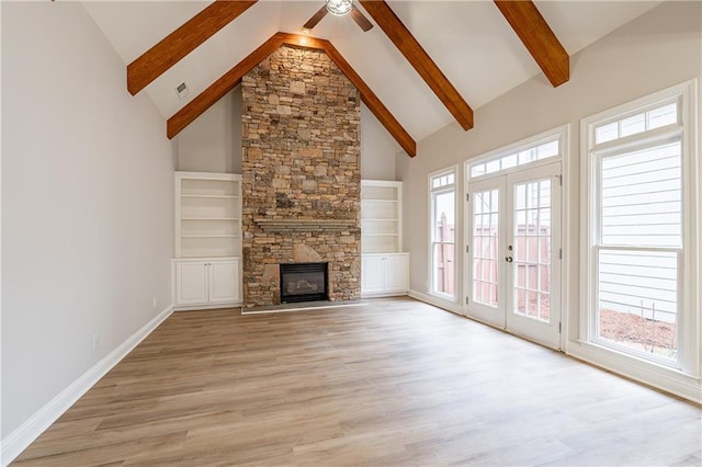 unfurnished living room featuring a stone fireplace, high vaulted ceiling, light hardwood / wood-style floors, beam ceiling, and french doors