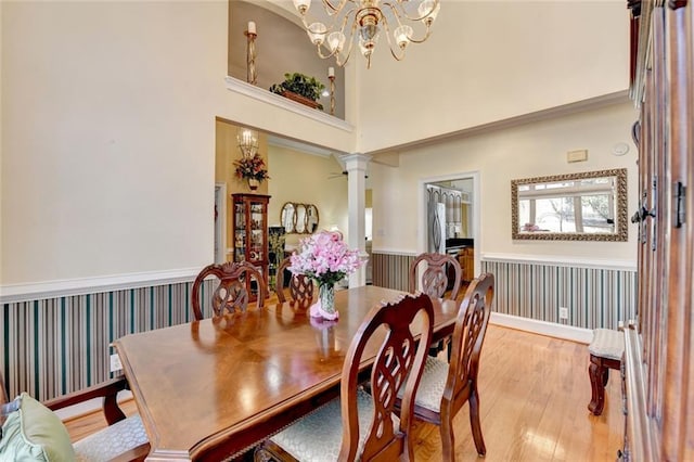 dining room featuring light wood-type flooring, wainscoting, ornate columns, wallpapered walls, and an inviting chandelier