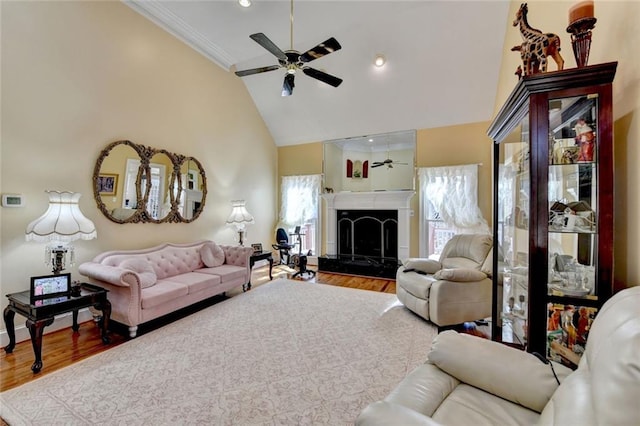 living room with a ceiling fan, ornamental molding, wood finished floors, a fireplace, and high vaulted ceiling