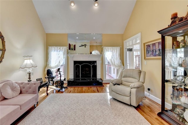 living room featuring high vaulted ceiling, baseboards, wood finished floors, and a tile fireplace