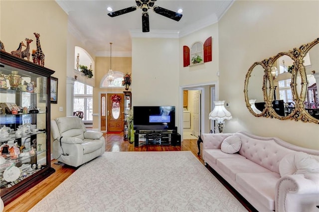 living area with a high ceiling, wood finished floors, a ceiling fan, ornamental molding, and decorative columns