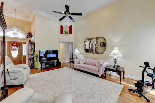 living room featuring crown molding, a towering ceiling, wood finished floors, baseboards, and ceiling fan with notable chandelier