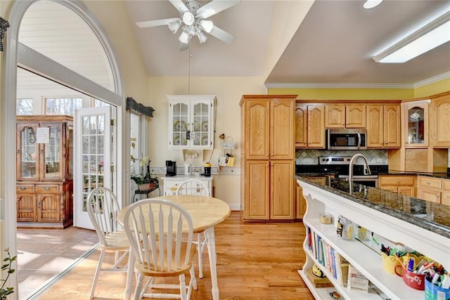 kitchen featuring dark stone counters, glass insert cabinets, stainless steel appliances, crown molding, and backsplash