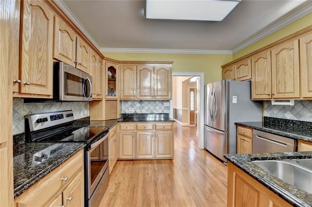 kitchen with stainless steel appliances, light wood-style flooring, decorative backsplash, ornamental molding, and dark stone countertops