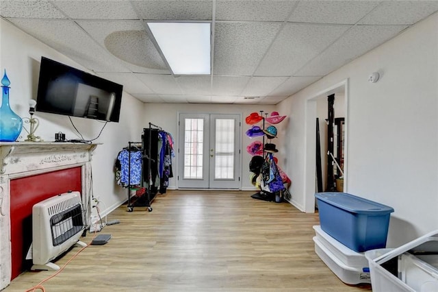 interior space featuring french doors, heating unit, wood finished floors, a drop ceiling, and baseboards