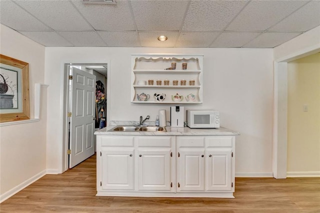 bar featuring white microwave, a drop ceiling, light wood-style flooring, a sink, and baseboards