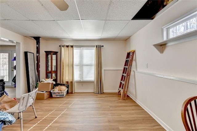 living area with a paneled ceiling, light wood-style floors, and baseboards