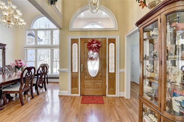 foyer entrance featuring a towering ceiling, light wood finished floors, baseboards, and a notable chandelier