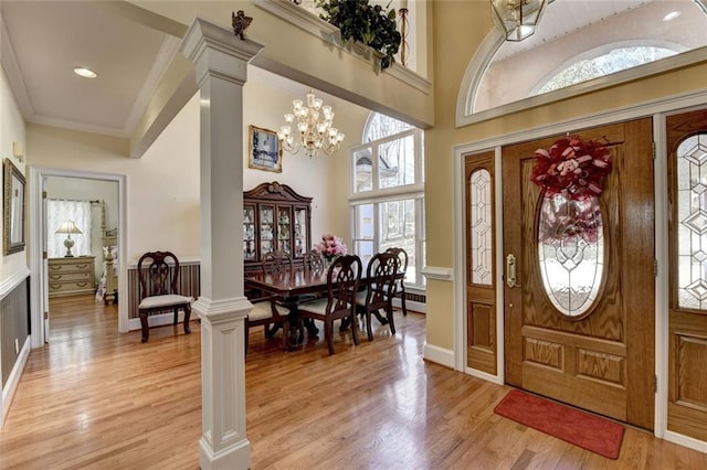 entrance foyer featuring light wood-type flooring, ornate columns, a notable chandelier, and crown molding