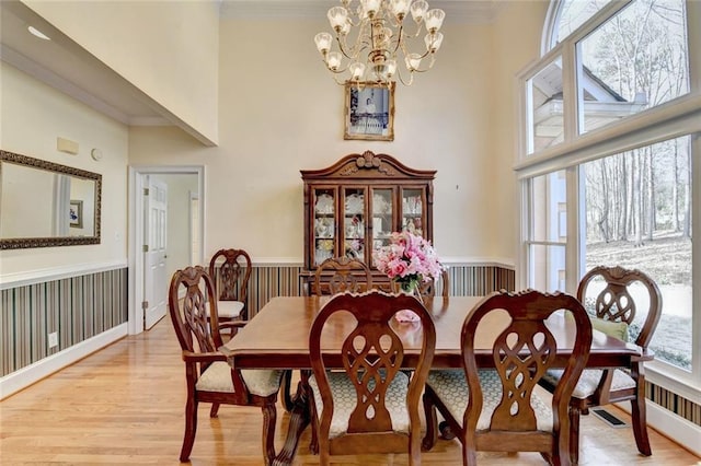 dining area with light wood-style flooring, a high ceiling, crown molding, and wainscoting