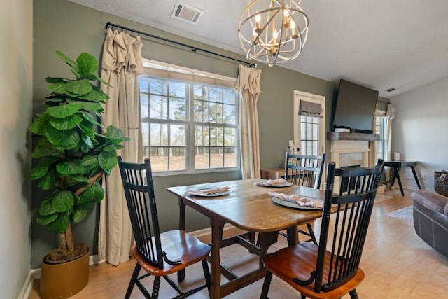 dining area with light wood finished floors, a fireplace, visible vents, and an inviting chandelier