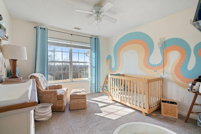 carpeted bedroom with a ceiling fan, a nursery area, visible vents, and a textured ceiling