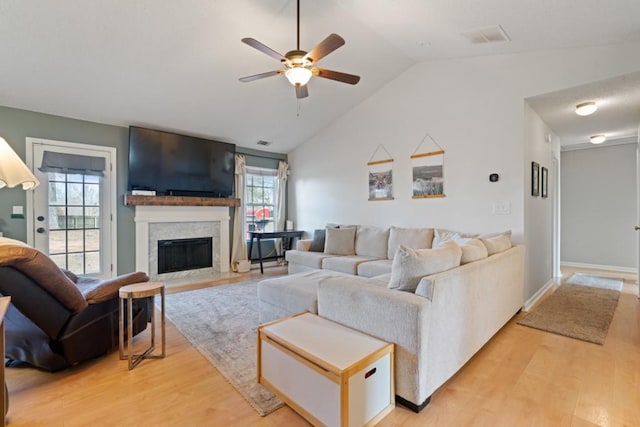 living room featuring lofted ceiling, light wood-type flooring, a fireplace with flush hearth, and visible vents