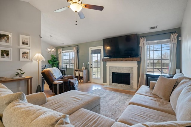 living room featuring a fireplace, lofted ceiling, visible vents, wood finished floors, and ceiling fan with notable chandelier