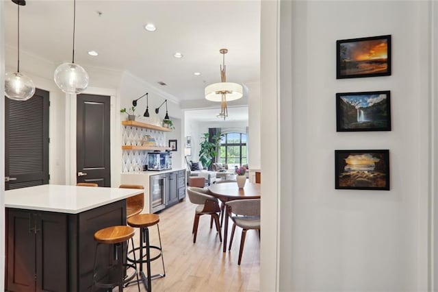 kitchen featuring light wood-style flooring, beverage cooler, a breakfast bar, light countertops, and ornamental molding