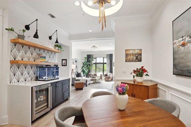 bar with wine cooler, a wainscoted wall, visible vents, ornamental molding, and a bar