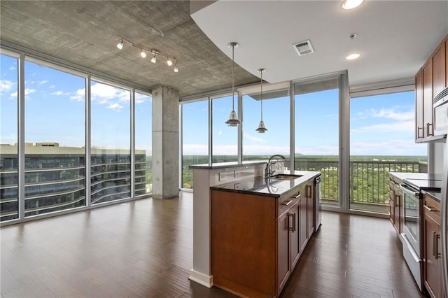 kitchen featuring a wall of windows, dark stone counters, hanging light fixtures, a kitchen island with sink, and electric range