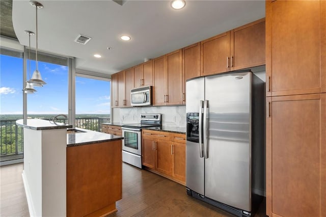 kitchen with hanging light fixtures, appliances with stainless steel finishes, dark stone countertops, and dark hardwood / wood-style flooring