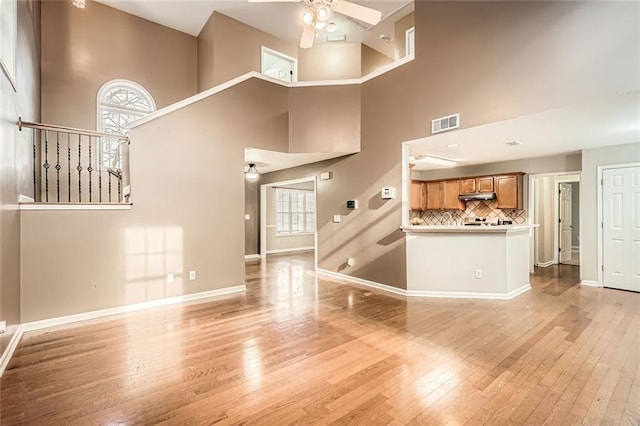 unfurnished living room with ceiling fan, light wood-type flooring, and a towering ceiling