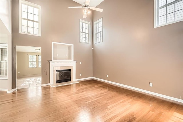 unfurnished living room with a high ceiling, a wealth of natural light, ceiling fan, and hardwood / wood-style floors