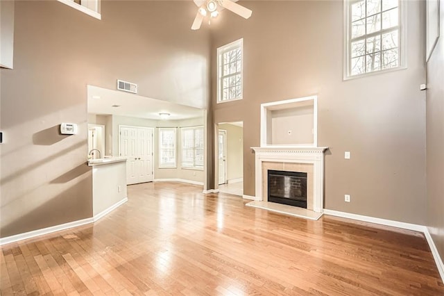 unfurnished living room with ceiling fan, light hardwood / wood-style floors, and a high ceiling