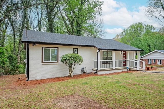 ranch-style home featuring covered porch, brick siding, roof with shingles, and a front yard
