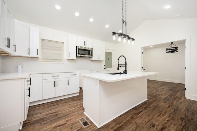 kitchen featuring a sink, stainless steel microwave, visible vents, a center island with sink, and white cabinetry