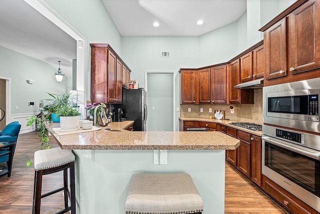 7731 Sleepy Lagoon Way, Flowery Branch, GA 30542 - kitchen featuring stainless steel appliances, under cabinet range hood, a peninsula, a breakfast bar area, and light stone counters