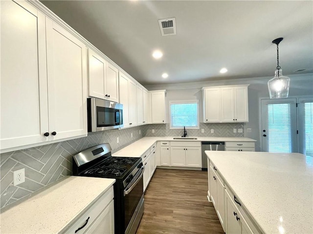 kitchen with pendant lighting, sink, appliances with stainless steel finishes, light stone countertops, and white cabinets