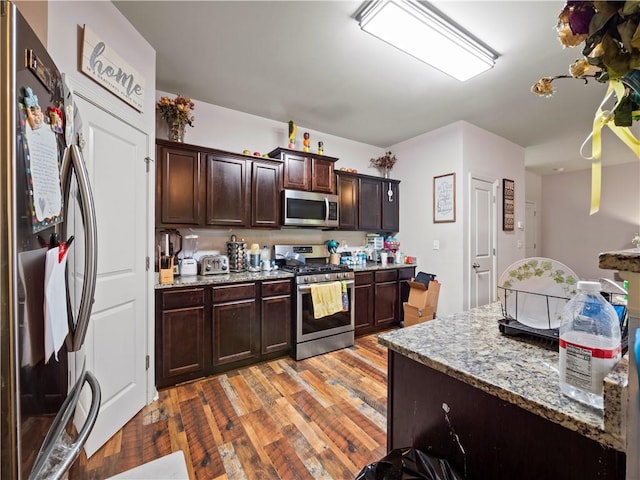 kitchen with light hardwood / wood-style floors, appliances with stainless steel finishes, dark brown cabinetry, and light stone counters