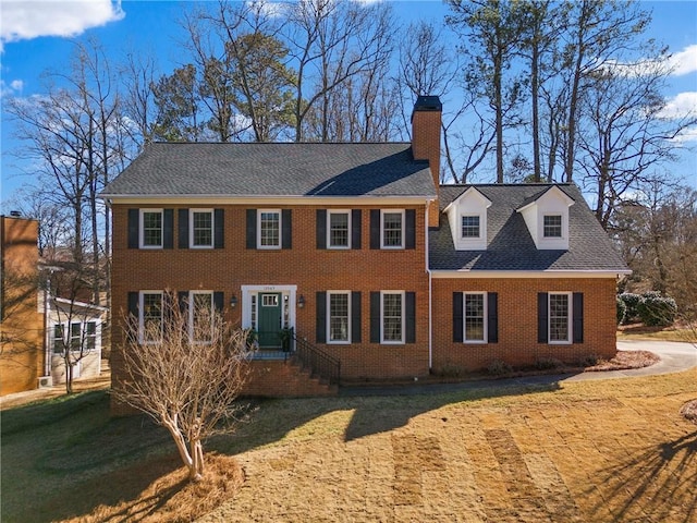 colonial inspired home with a shingled roof, a chimney, a front lawn, and brick siding