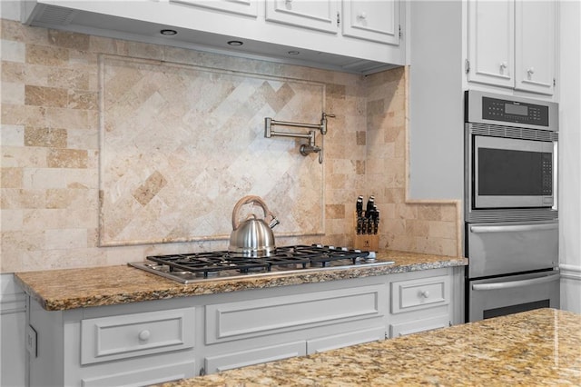 kitchen with appliances with stainless steel finishes, light stone countertops, white cabinetry, and tasteful backsplash