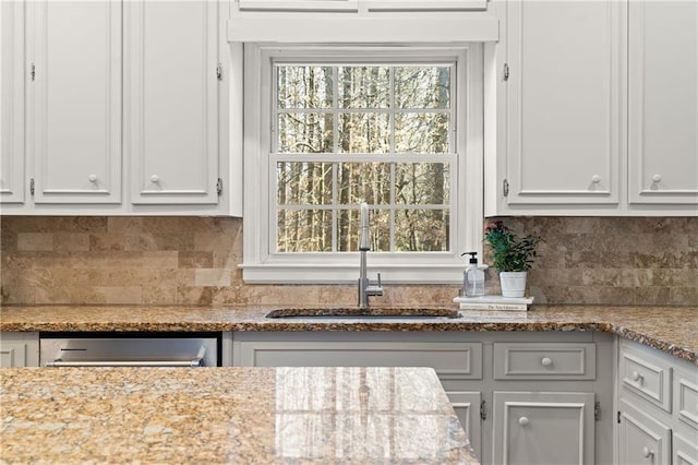 kitchen with light stone counters, white cabinets, a sink, and backsplash