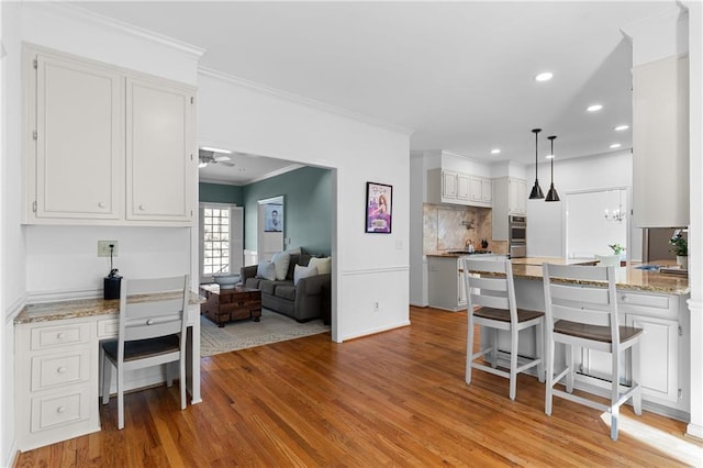 kitchen featuring light wood finished floors, decorative backsplash, a ceiling fan, ornamental molding, and a peninsula