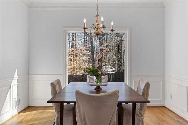 dining area with crown molding, a wainscoted wall, a chandelier, and light wood-style floors