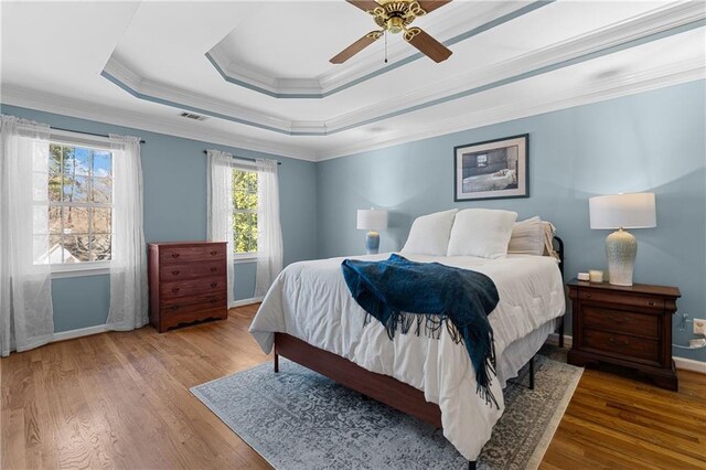 bedroom featuring a tray ceiling, visible vents, ornamental molding, wood finished floors, and baseboards