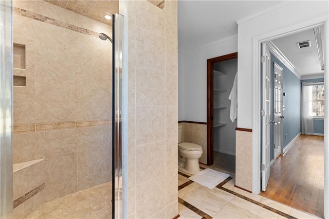 bathroom with visible vents, toilet, ornamental molding, a shower stall, and tile walls