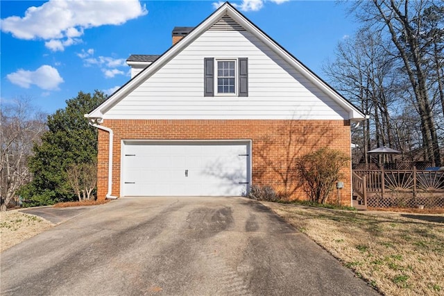 view of side of property with a deck, brick siding, driveway, and a chimney