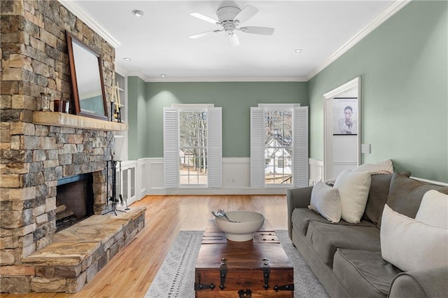 living area featuring a wainscoted wall, crown molding, a fireplace, and light wood-style floors