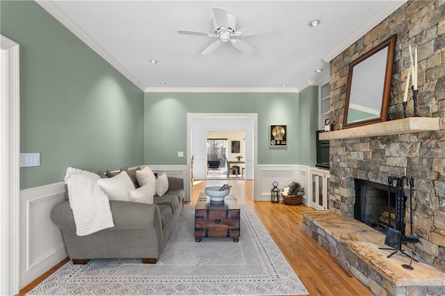 living area with a wainscoted wall, a stone fireplace, wood finished floors, and crown molding