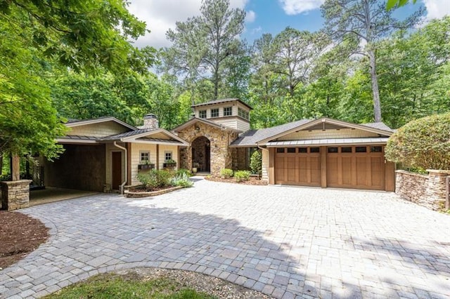 view of front of property featuring a garage, stone siding, decorative driveway, and a chimney