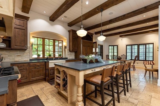 kitchen with stone tile floors, a sink, a wealth of natural light, decorative backsplash, and dark countertops