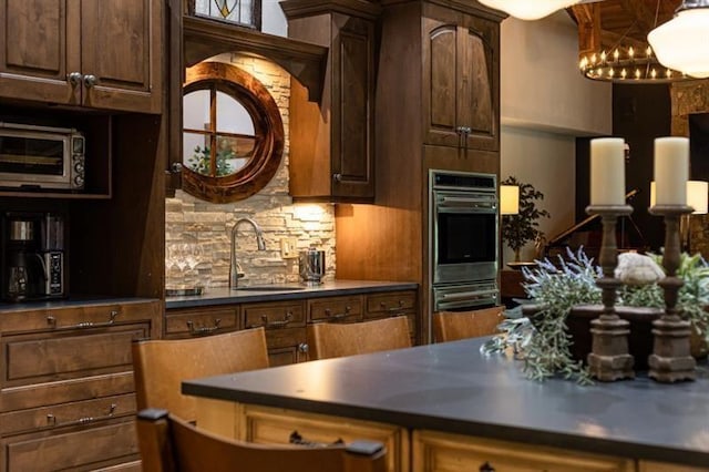 kitchen with dark countertops, an inviting chandelier, decorative backsplash, and a sink