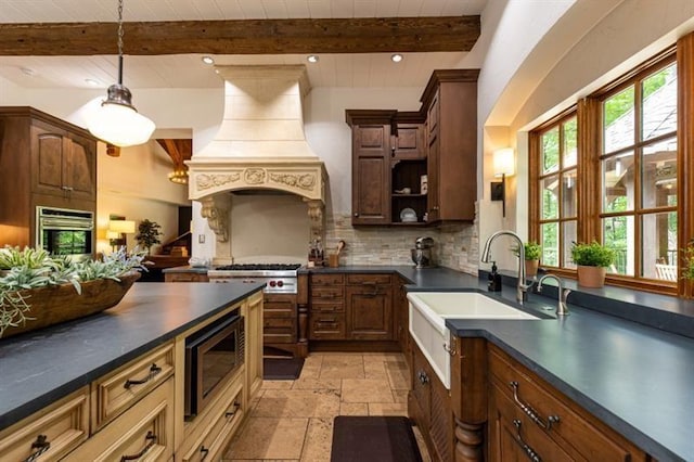 kitchen featuring stainless steel appliances, premium range hood, dark countertops, and a sink