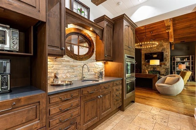 kitchen featuring a fireplace, stone tile flooring, double oven, a sink, and wooden ceiling