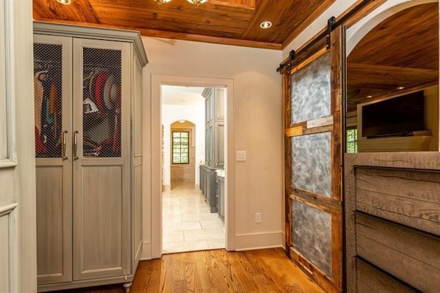 hall featuring arched walkways, a barn door, wood finished floors, wooden ceiling, and baseboards