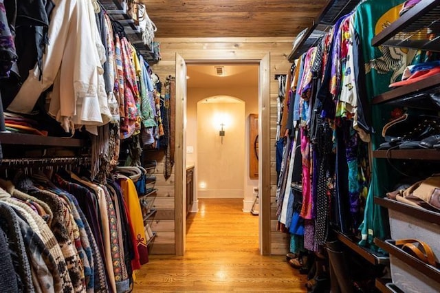 walk in closet with arched walkways and wood finished floors