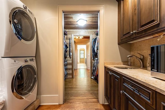 clothes washing area featuring cabinet space, light wood-style flooring, stacked washing maching and dryer, and a sink